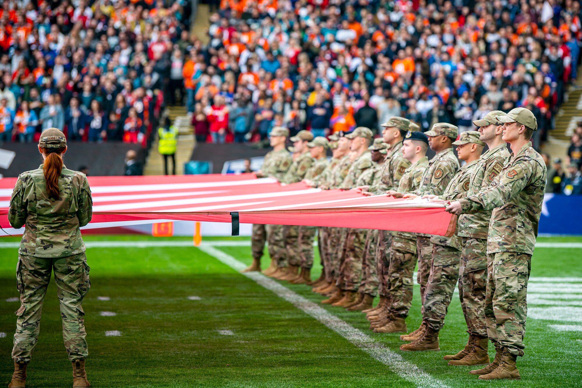 Airmen from the 501st Combat Support Wing hold an American flag during the national anthem at Wembley Stadium, in London, England, Oct. 30, 2022. Approximately 70 uniformed personnel represented the U.S. Air Force and nation by unveiling an American flag during the pre-game ceremonies of the Jacksonville Jaguars and Denver Broncos NFL game. (U.S. Air Force photo by Staff Sgt. Eugene Oliver)
