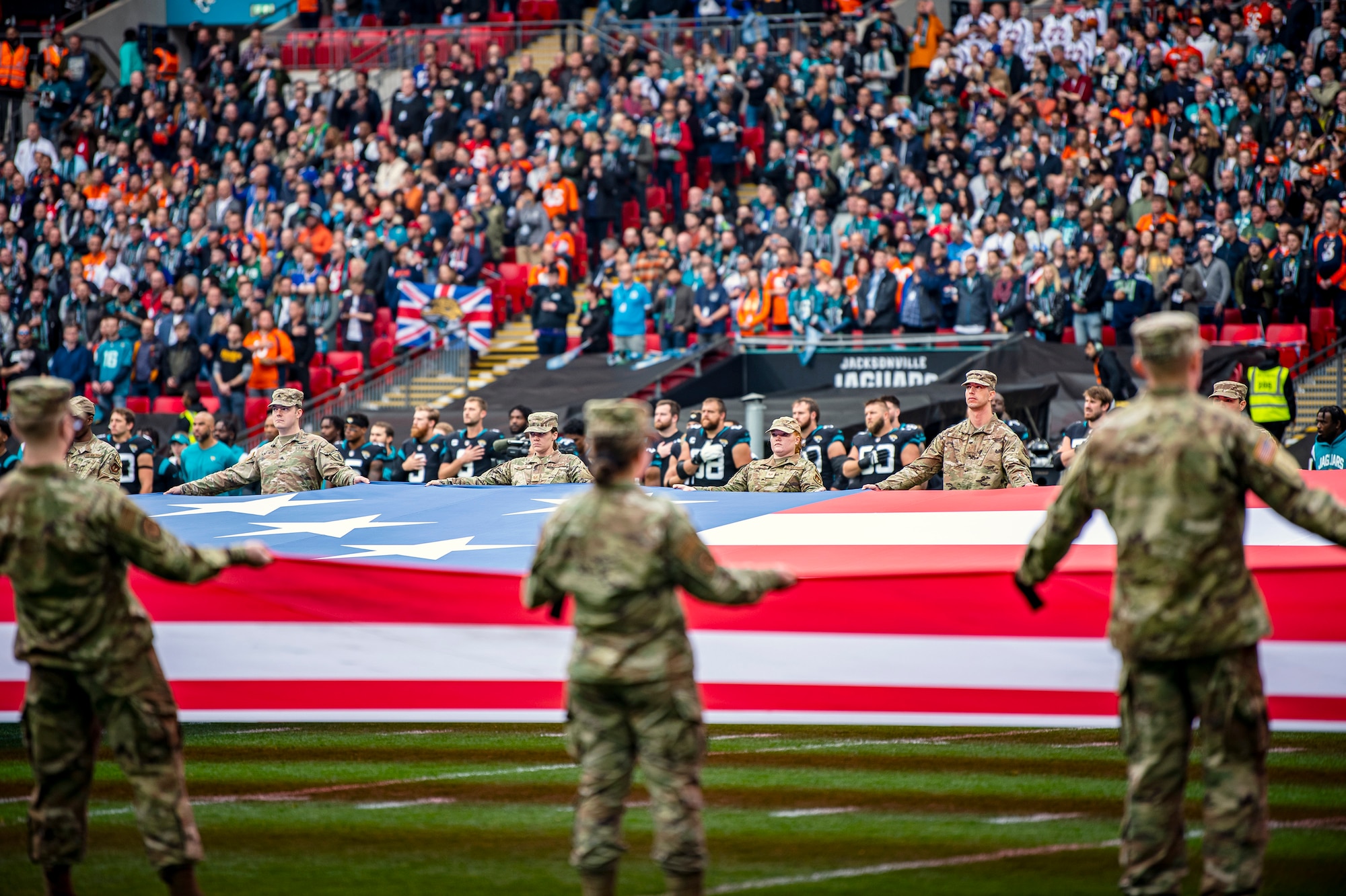 Airmen from the 501st Combat Support Wing unveil an American flag during the national anthem at Wembley Stadium, in London, England, Oct. 30, 2022. Approximately 70 uniformed personnel represented the U.S. Air Force and nation by unveiling an American flag during the pre-game ceremonies of the Jacksonville Jaguars and Denver Broncos NFL game. (U.S. Air Force photo by Staff Sgt. Eugene Oliver)