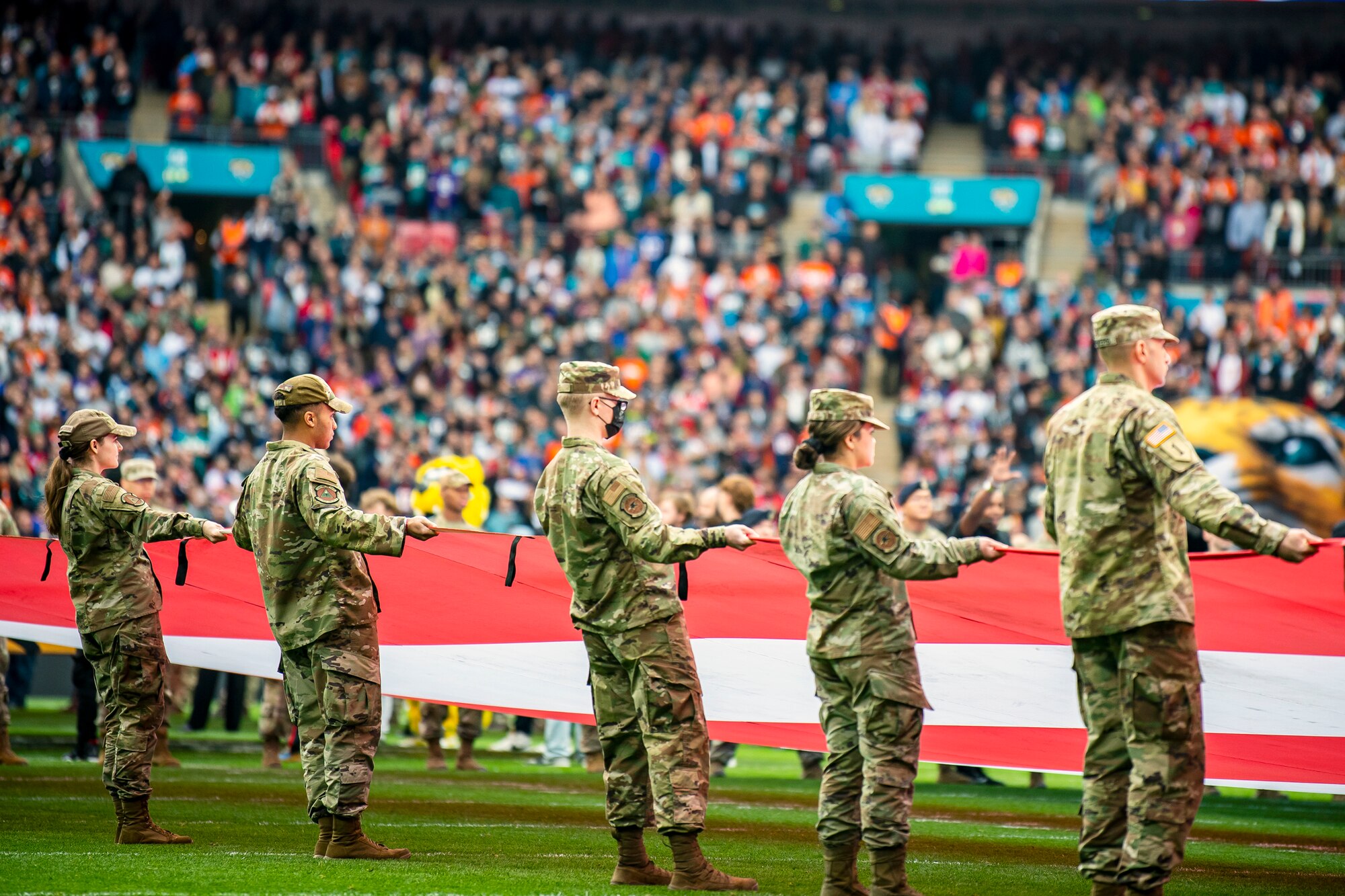 Airmen from the 501st Combat Support Wing unveil an American flag during the national anthem at Wembley Stadium, in London, England, Oct. 30, 2022. Approximately 70 uniformed personnel represented the U.S. Air Force and nation by unveiling an American flag during the pre-game ceremonies of the Jacksonville Jaguars and Denver Broncos NFL game. (U.S. Air Force photo by Staff Sgt. Eugene Oliver)