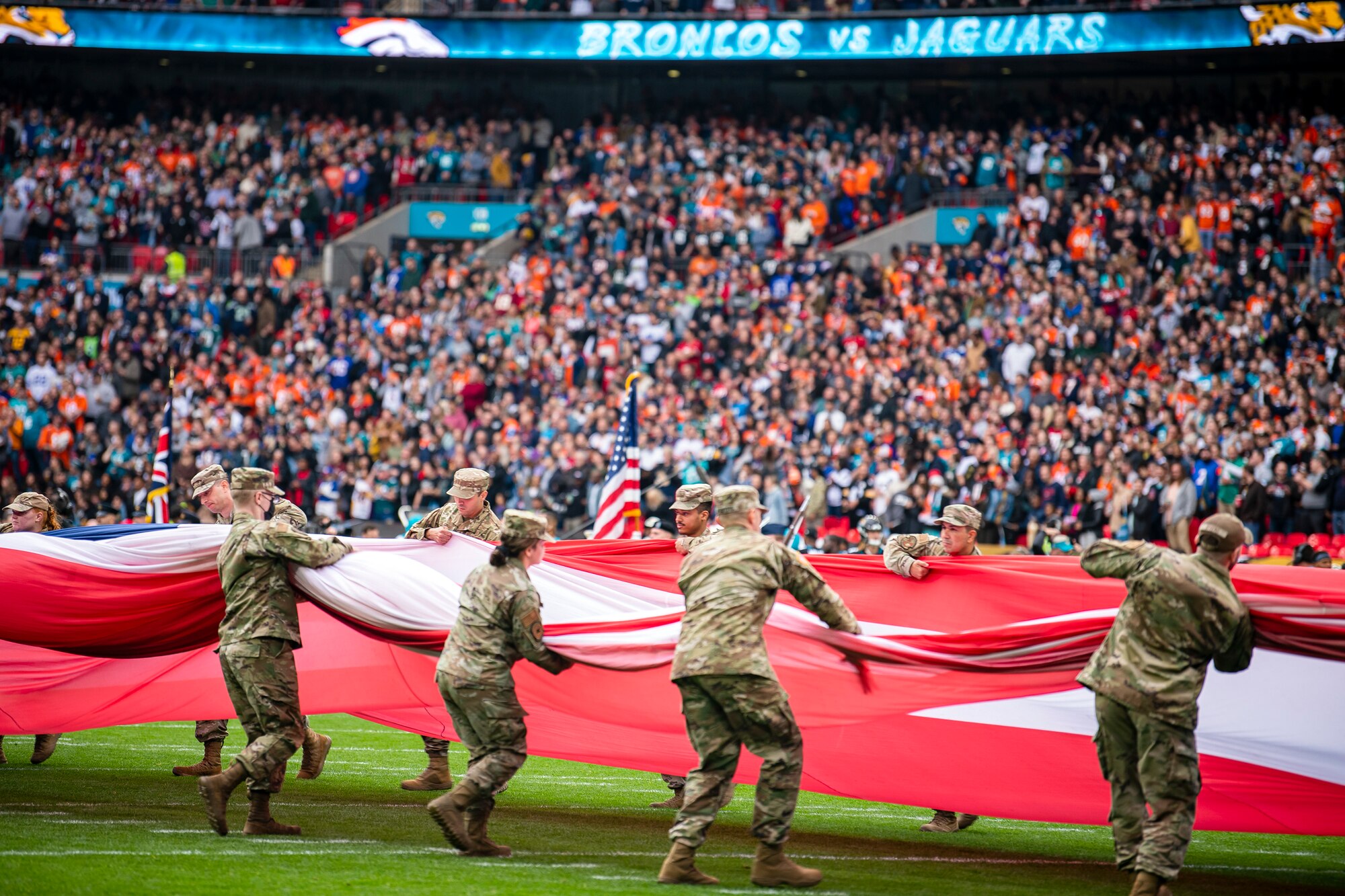 Airmen from the 501st Combat Support Wing pull together an American flag following the national anthem at Wembley Stadium, in London, England, Oct. 30, 2022. Approximately 70 uniformed personnel represented the U.S. Air Force and nation by unveiling an American flag during the pre-game ceremonies of the Jacksonville Jaguars and Denver Broncos NFL game. (U.S. Air Force photo by Staff Sgt. Eugene Oliver)