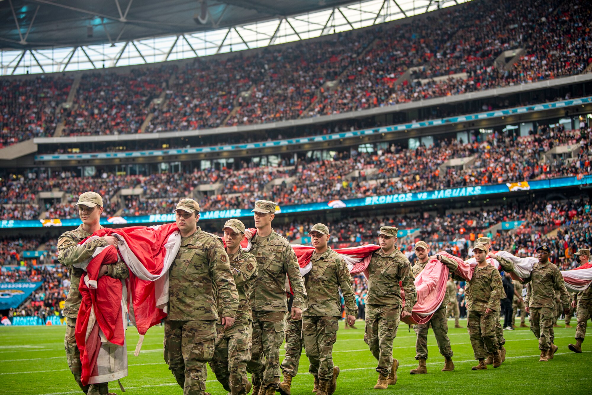 Airmen from the 501st Combat Support Wing carry an American flag off the field following the national anthem at Wembley Stadium, in London, England, Oct. 30, 2022. Approximately 70 uniformed personnel represented the U.S. Air Force and nation by unveiling an American flag during the pre-game ceremonies of the Jacksonville Jaguars and Denver Broncos NFL game. (U.S. Air Force photo by Staff Sgt. Eugene Oliver)