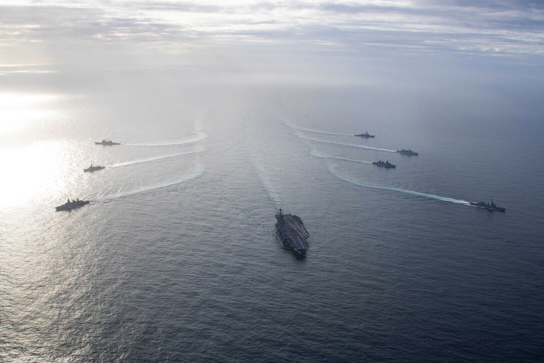 American ships sail in a curved formation in the ocean with foreign ships.