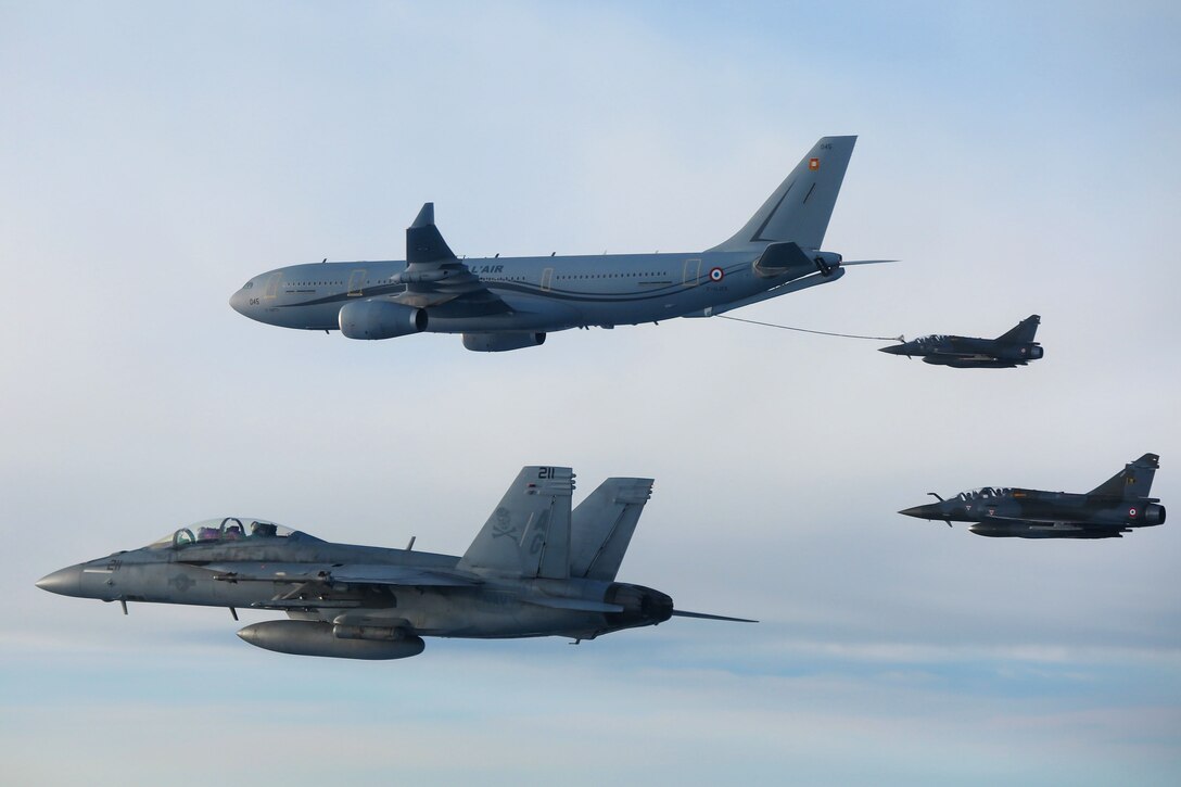 Four aircraft fly in formation, with a boom extending from the largest one to another.