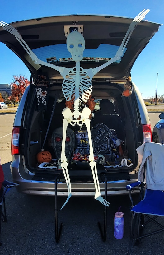 A skeleton hangs off a car trunk with treats positioned below.