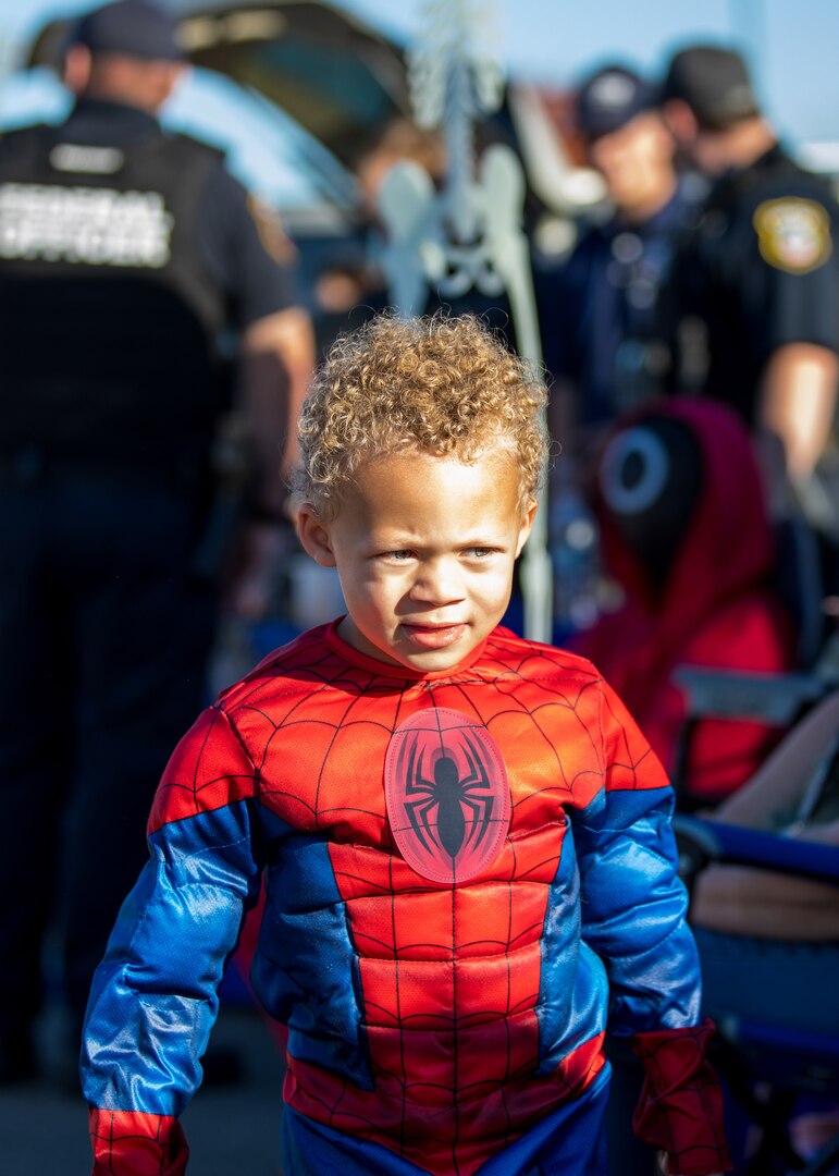 A child dressed in a Spiderman costume. He has blond curly hair and is dark skinned.