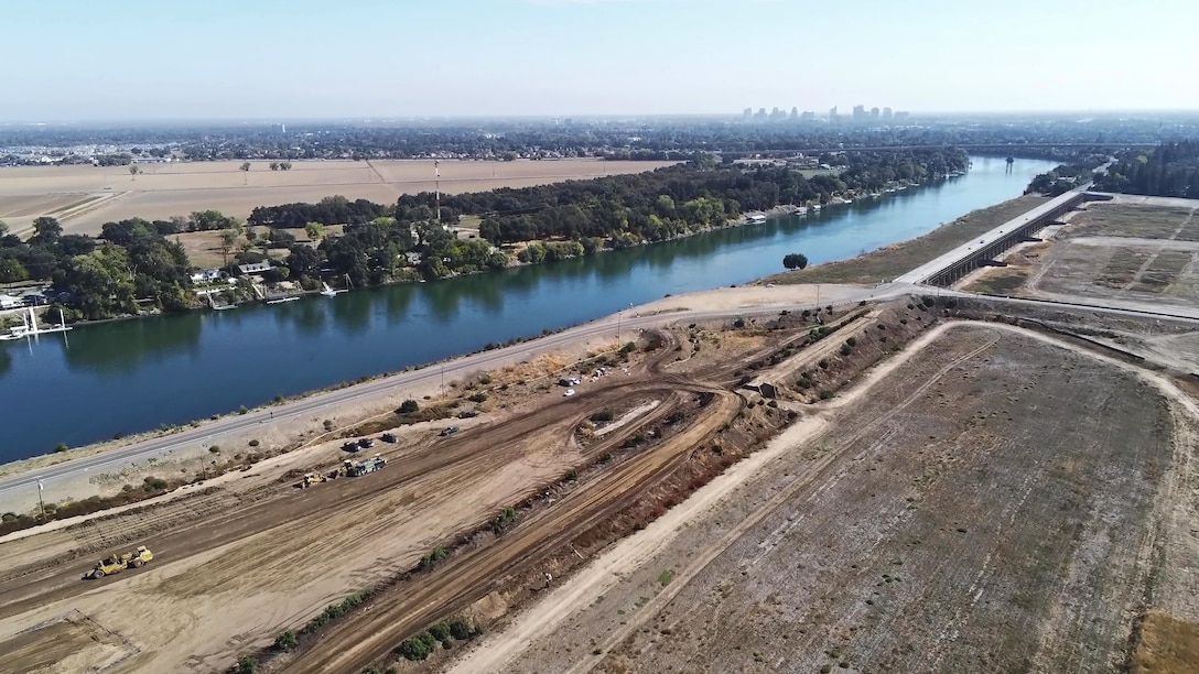 Aerial image of contractors and heavy equipment preparing the construction site for the Sacramento Weir Widening Project along the west bank of the Sacramento River, California.