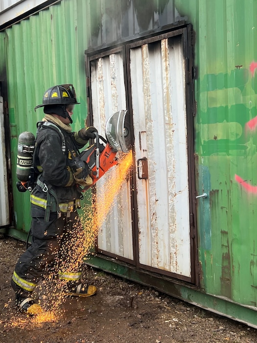 A newly hired fire fighter conducts forcible entry procedures during a structure fire as part of a training live fire evolution at Lake Superior College's Emergency Response Training Center, Duluth, Minnesota, October 27, 2022.