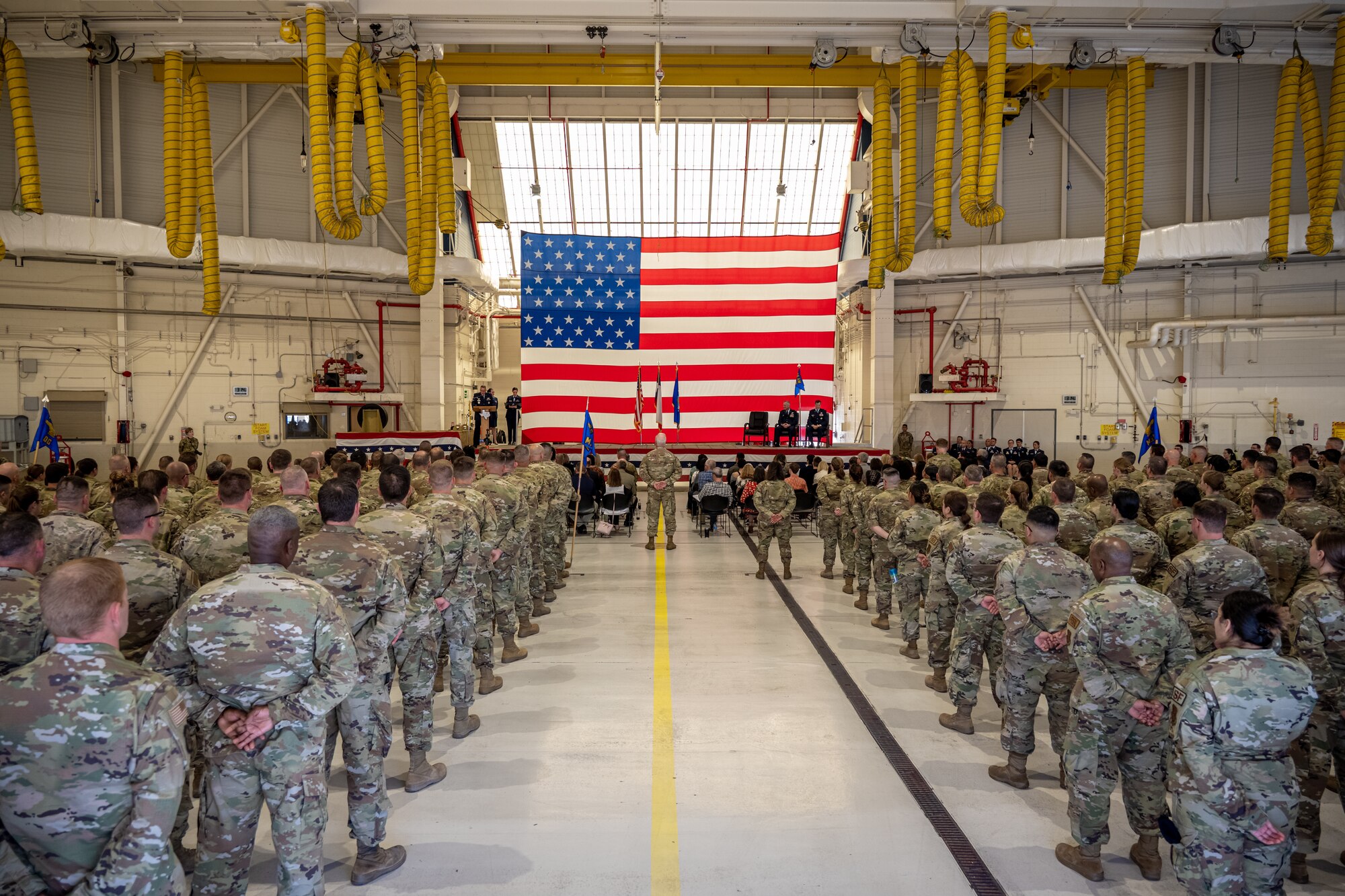 Military troops stand in formation before a change of command ceremony in a hangar.