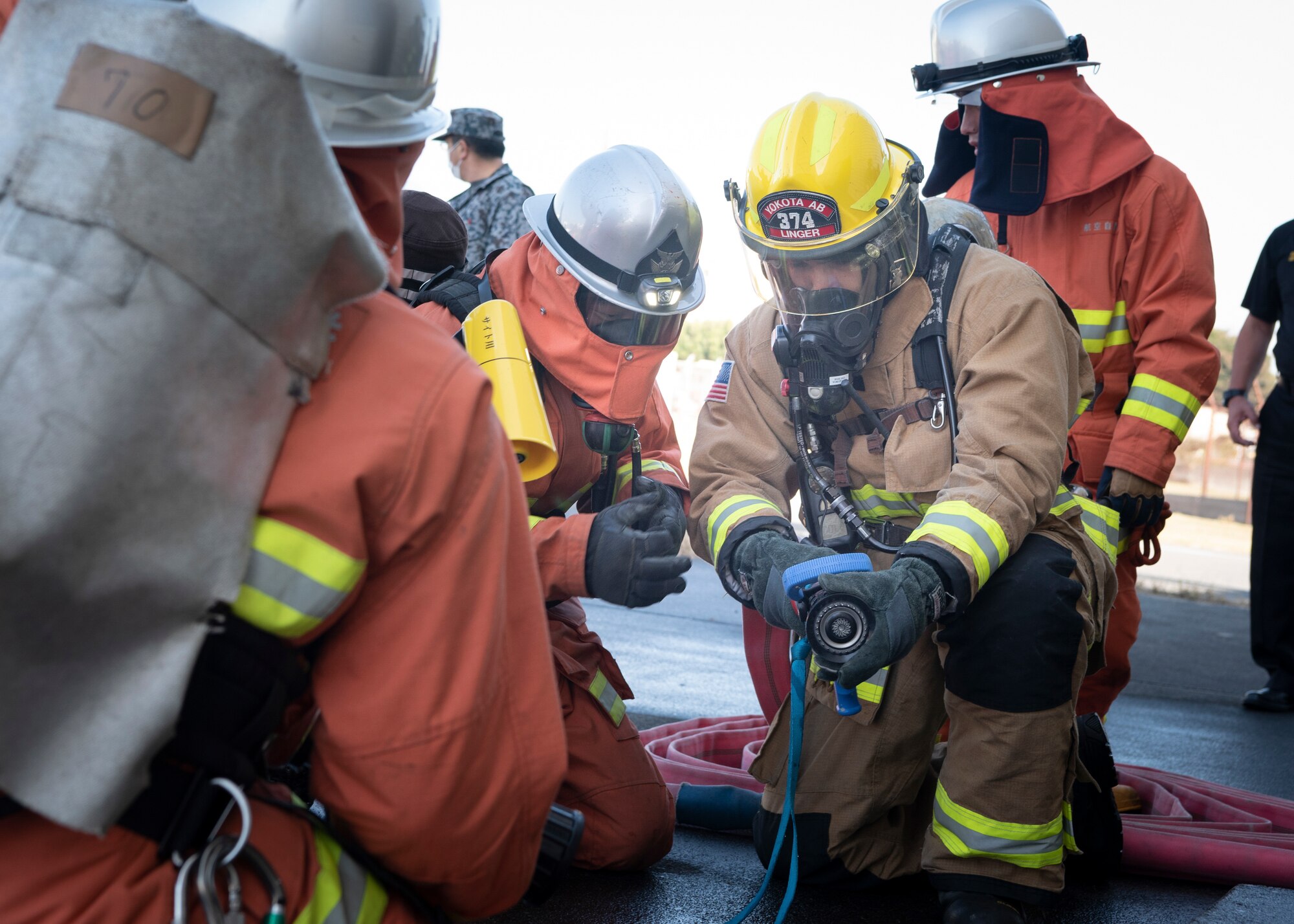 A firefighter with the Japanese Air Self-Defense Force, left, teaches Airman 1st Class Jeremy Linger, 374th Civil Engineer Squadron firefighter, right, how to use a Japanese fire hose during a bilateral training at Yokota Air Base, Japan, Oct. 28, 2022.