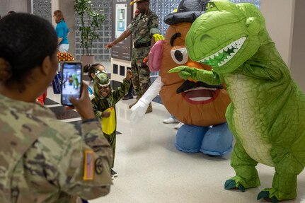 A Soldier snaps a photo of a student from a nearby childcare center as he poses with Barry W. Hoffman, U.S. Army Financial Management Command deputy to the commander, dressed as Mr. Potato Head, and Command Sgt. Maj. Kenneth F. Law, in a dinosaur costume, at the Maj. Gen. Emmett J. Bean Federal Center Oct. 31, 2022. Students from the childcare center were able to return to their annual Halloween parade tradition for the first time since the COVID-19 pandemic. (U.S. Army photo by Mark R. W. Orders-Woempner)