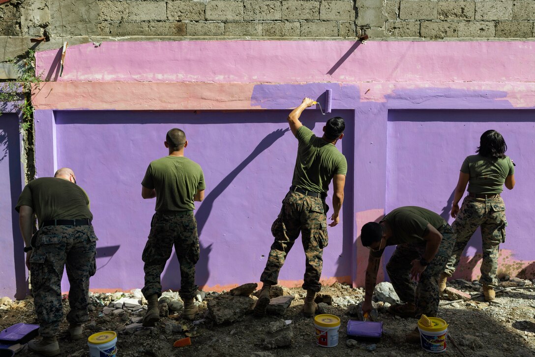 Marines paint an outdoor wall purple.