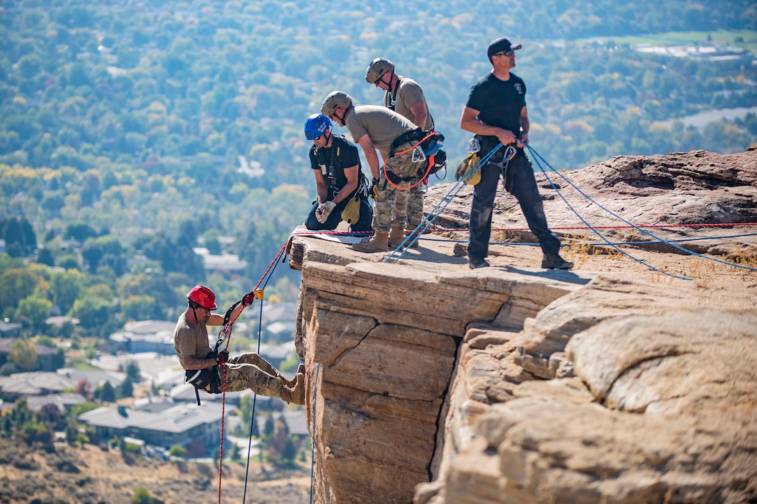 A guardsman rappels from a cliff as fellow service members and firefighters assist from above.