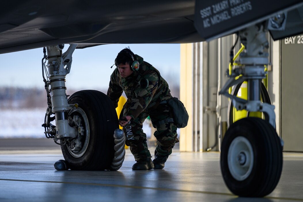 U.S. Air Force Staff Sgt. Diego Amezcua, 355th Aircraft Maintenance Unit avionics specialist, places a chock around an F-35A Lightning II wheel during a mini-generation on Eielson Air Force Base, Alaska, Oct. 26, 2022.