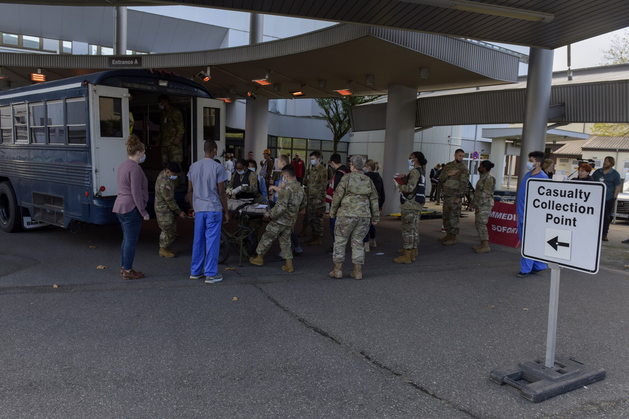 Many people in a military uniform help a patient, being played by an actor, out of an ambulatory bus on a litter.