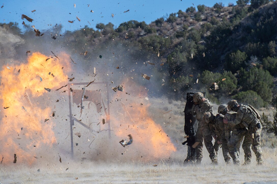 Soldiers crouch to the side as a door explodes, setting off debris and fire during a demonstration.