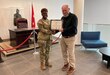 David Pagano, the 405th Army Field Support Brigade’s Logistics Civil Augmentation Program representative for the Wiesbaden area of operations, receives a cross-organizational award signed by U.S. Army Garrison Wiesbaden’s former commander and presented to him by the 405th AFSB commander, Col. Crystal Hills, at the U.S. Army Europe and Africa headquarters, Nov. 4. (Photo by SFC Guido Fermin)