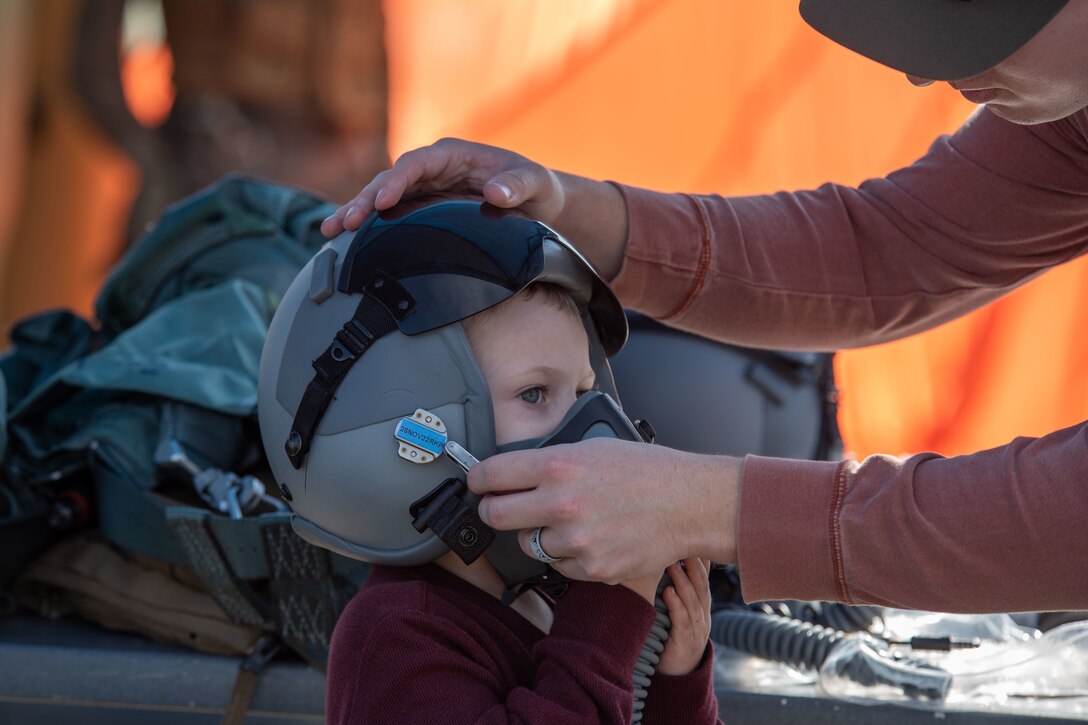 A child gets help trying on a pilot's helmet.