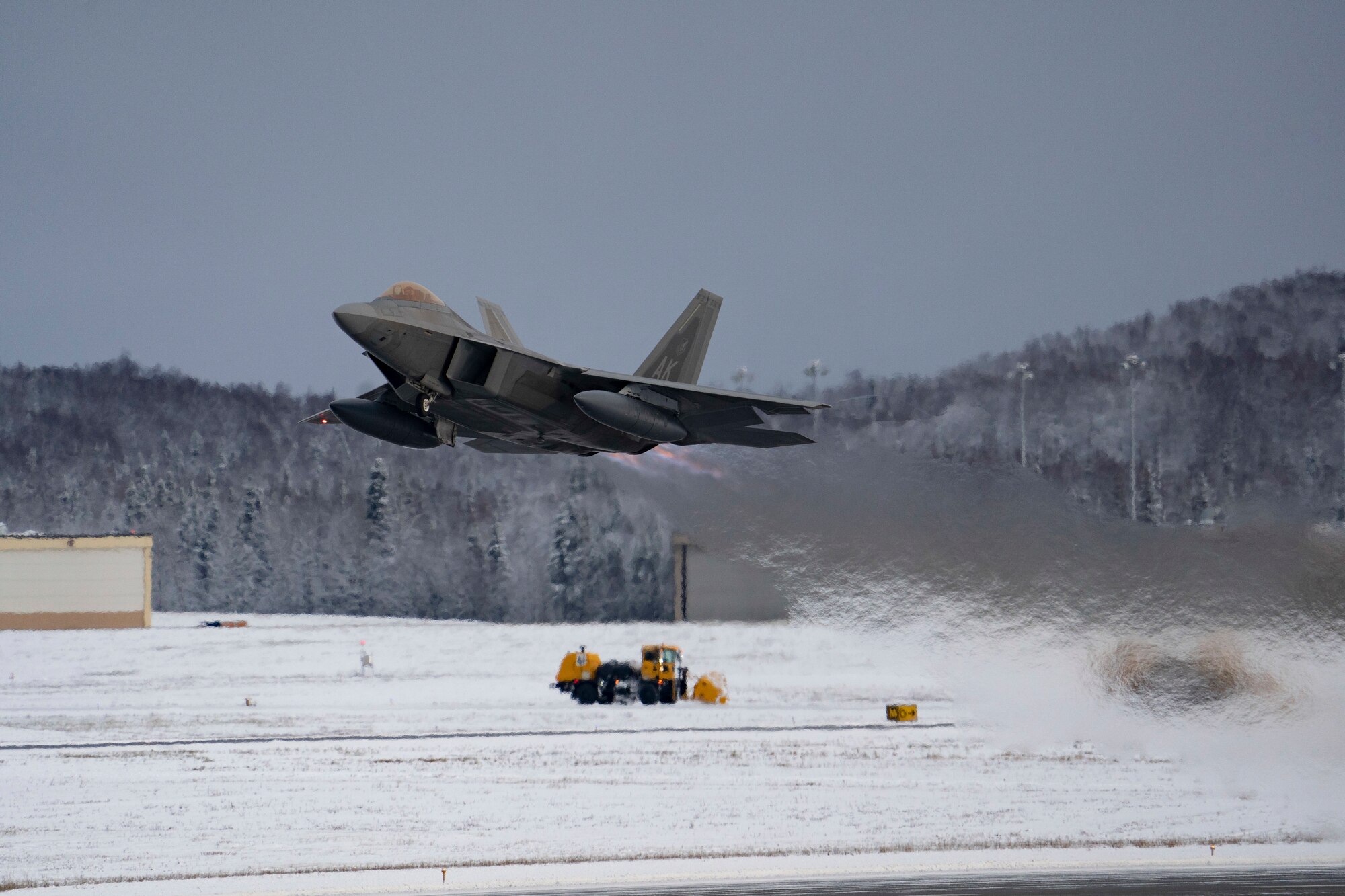 An F-22 Raptor and a snow plow during an aircraft launch