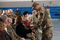 Man in military uniform hands a bouquet of flowers to a woman