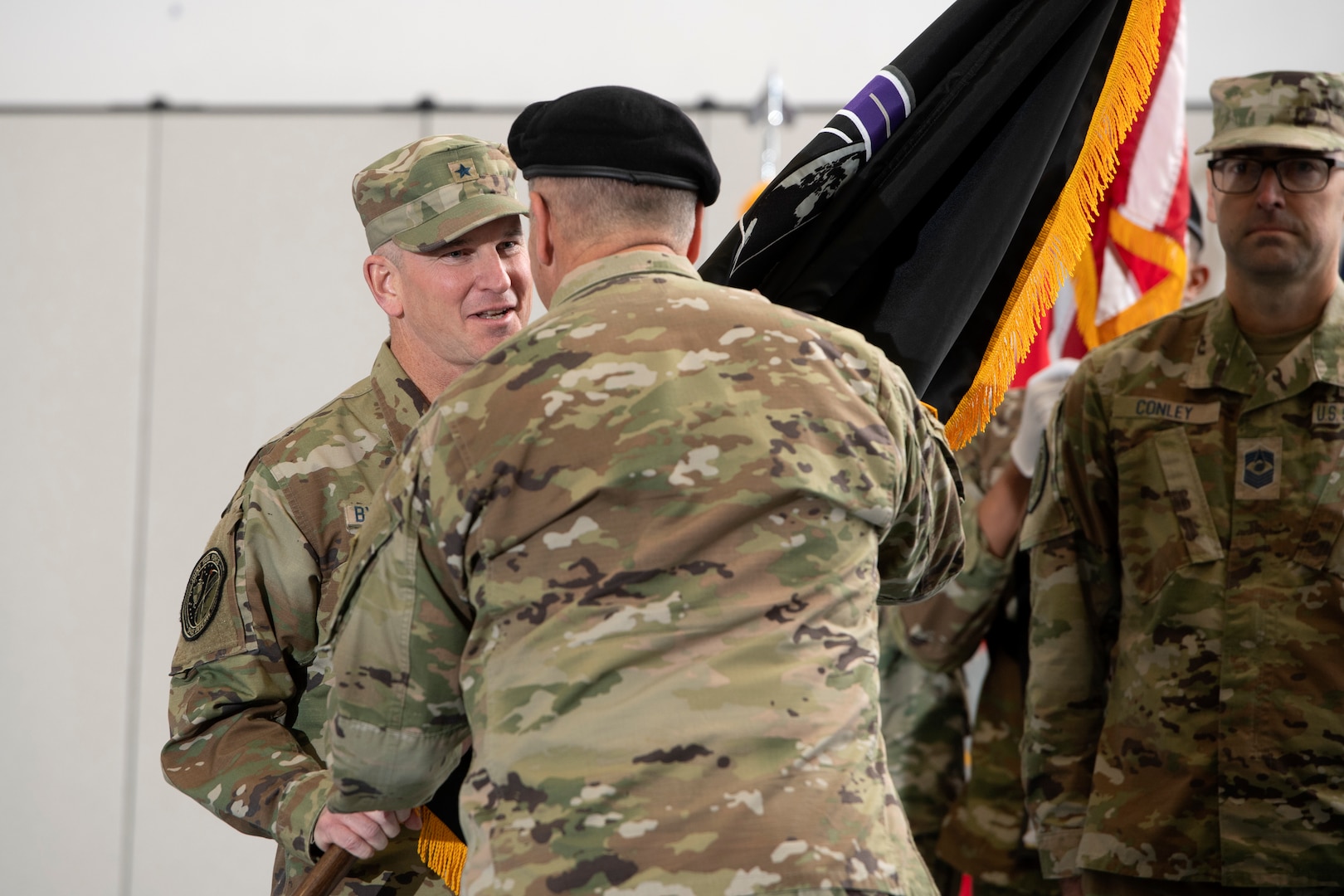 Man in military uniform hands flag to man in military uniform