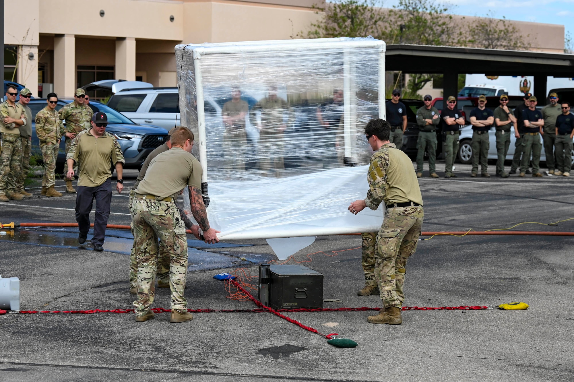 Air Force airmen carry an impromptu made large box made of PVC piping and wrapped in plastic wrap