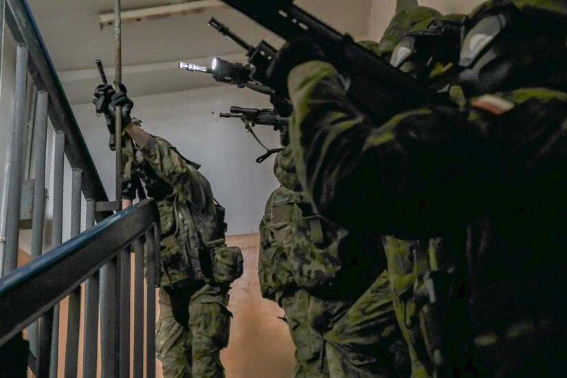 Troops with guns move up a stairway.