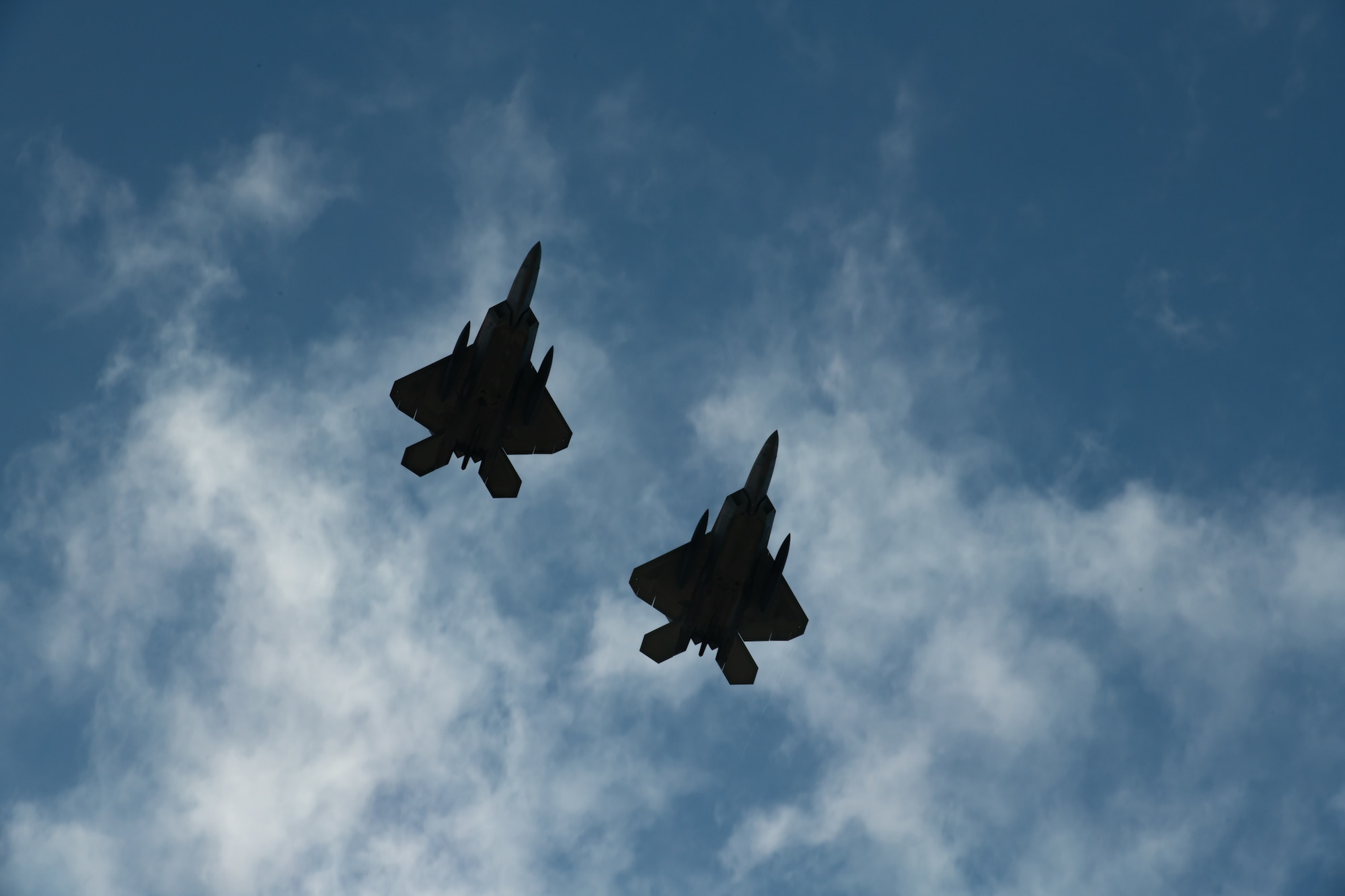Two F-22 Raptors fly overhead. Only their silhouettes can be seen.
