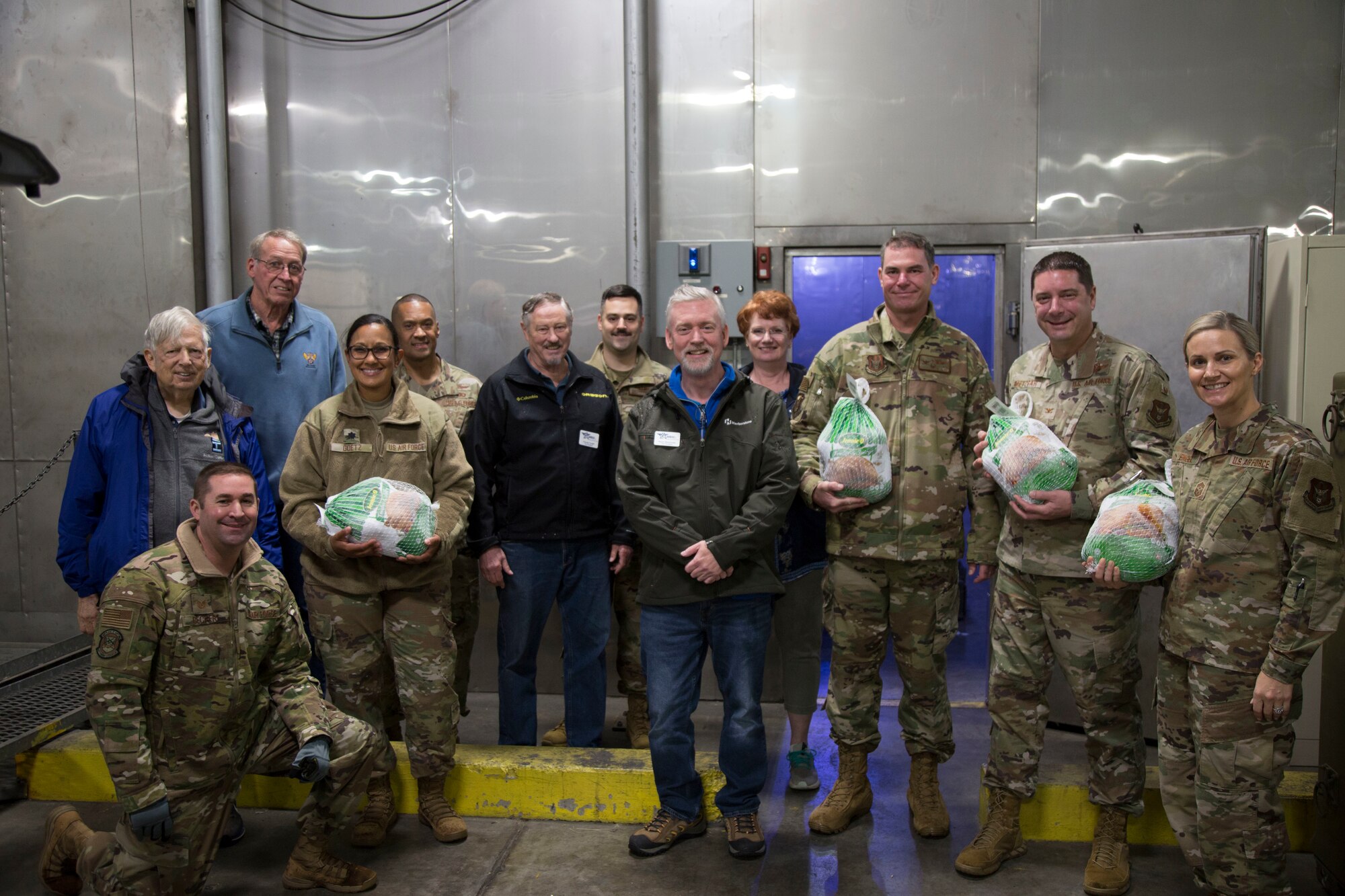 446th AW leadership in uniform with Air Force Association McChord Field Chapter pose holding turkeys in front of a walk in freezer.