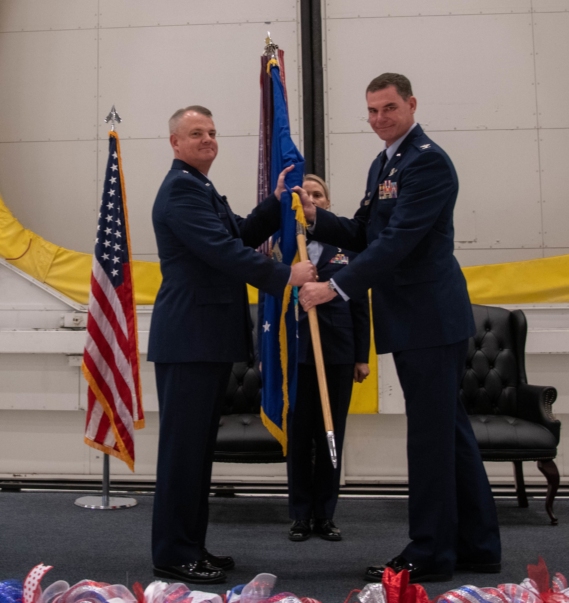 Two men in Air Force uniforms holding a flag guidon between them looking at the camera.