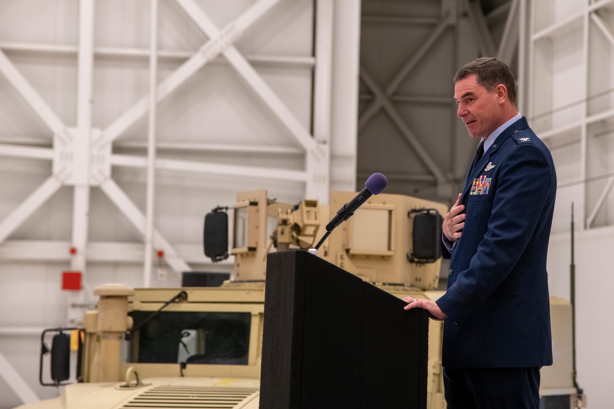 Man in Air Force uniform standing at a podium giving a speech in an aircraft hangar