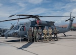 Six military personnel stand in front of a newly delivered HH-60W helicopter at an airfield.