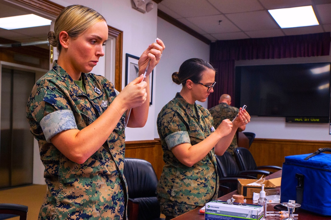 Two sailors hold syringes while preparing to administer vaccines.