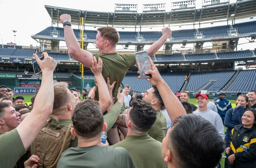 U.S. Marine Corps Lance Corporal Aidan Berne, Guard at Marine Barracks Washington, is lifted in celebration after winning a push-up competition hosted by the Washington Nationals baseball team on Oct. 28, 2022, at Nationals Park in Washington, D.C. Participants completed as many push-ups as possible until the last person remaining was announced the winner. (U.S. Air Force photo by Jason Treffry)