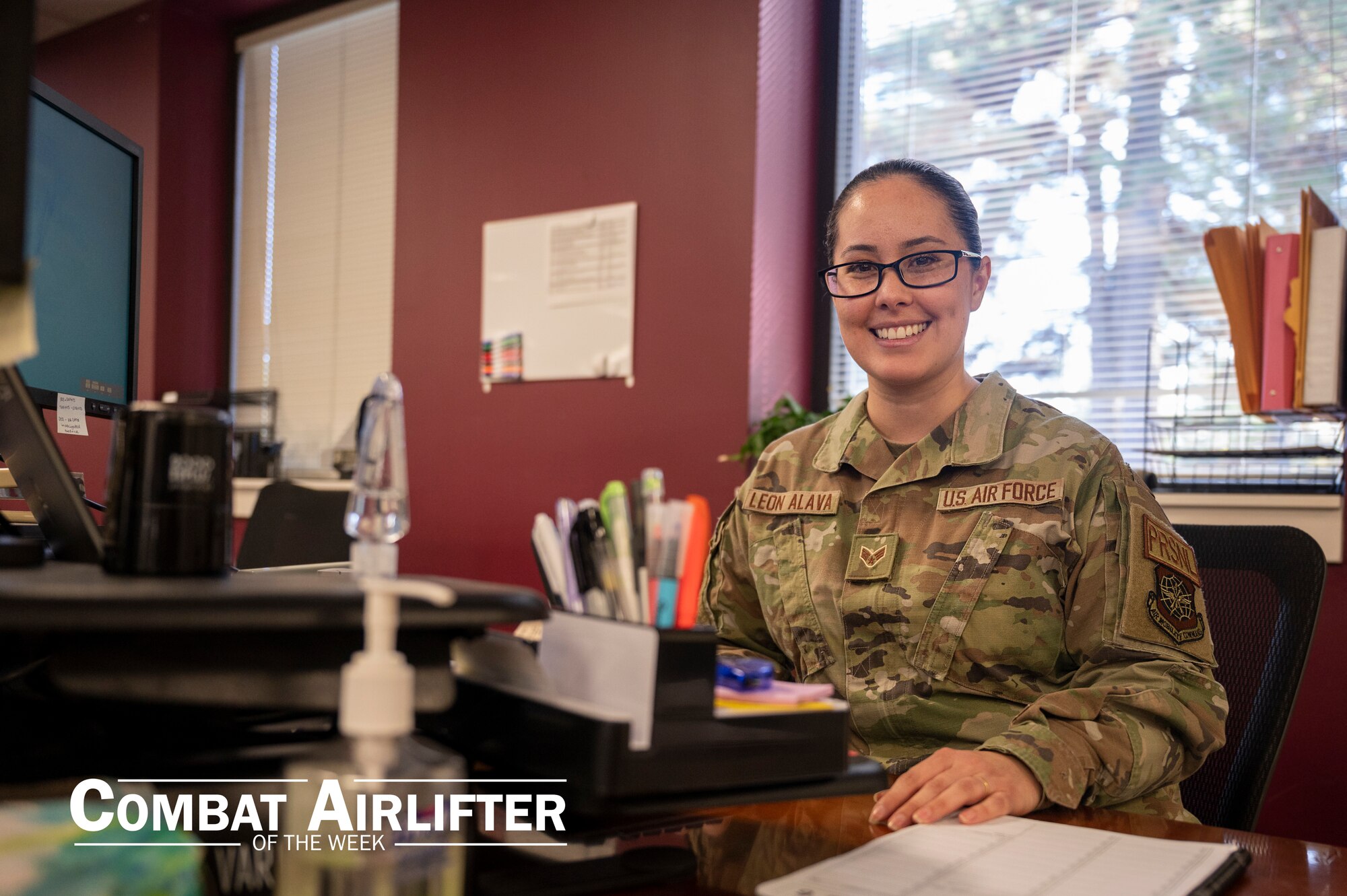 A woman in uniform sits at a desk and poses for a photo