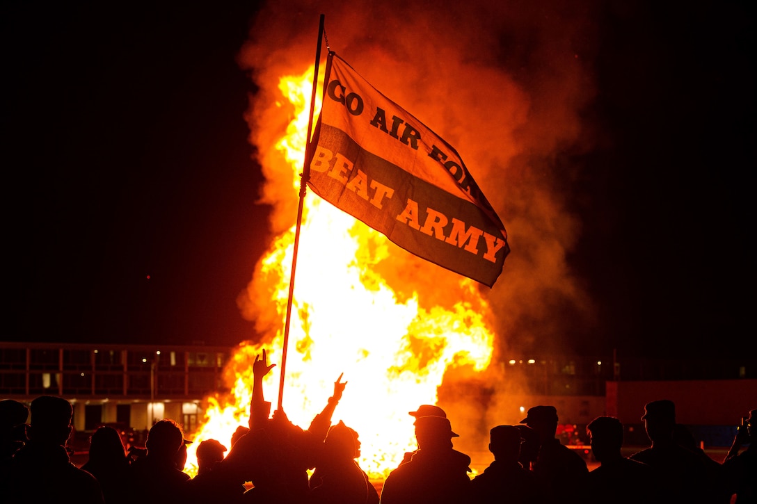 Air Force cadets gather around a bonfire holding a large flag saying 'Beat Army.'