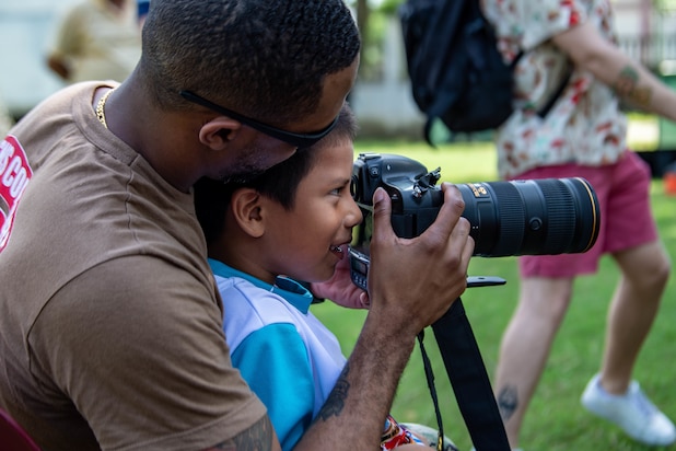 Mass Communication Specialist 1st Class Don White, from Norfolk, Virginia, attached to the hospital ship USNS Comfort (T-AH 20), shows a child from the orphanage Hugar de Niños San Ramon the view through a camera in Puerto Cortes, Honduras, Nov. 5, 2022.
