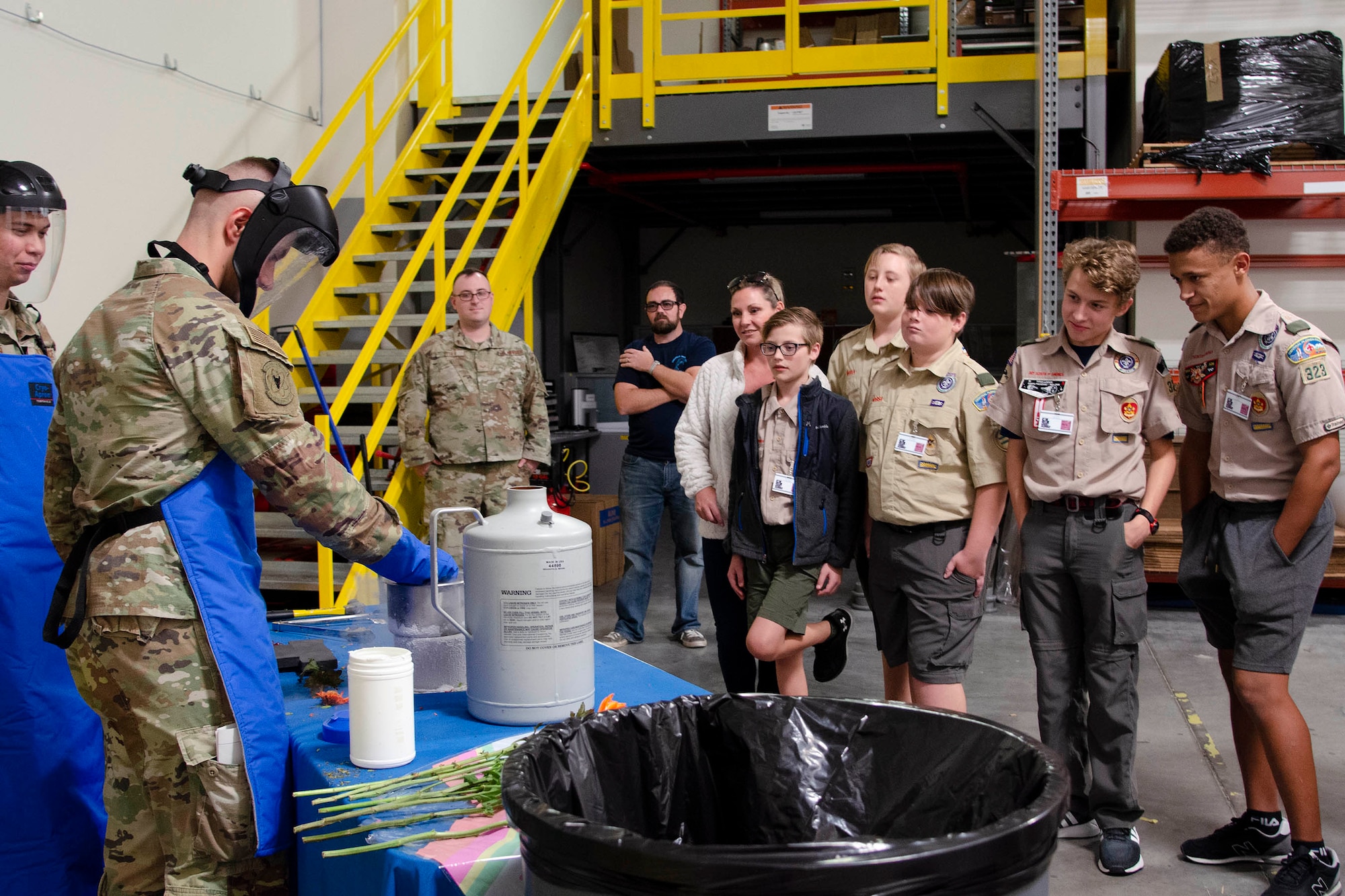 Airman Zachary Maga, a scientific applications specialist at the U.S. Air Force Radiochemistry Lab, demonstrate what happens when a carnation is placed into a container of liquid nitrogen, as Boy Scouts from around Central Florida observe the experiment.  Maga and his co-worker, Staff Sgt. Albert Silvain Jr., (far left) volunteered their time to help the scouts earn the Nuclear Science Merit Badge at Patrick Space Force Base, Fla., Oct. 22, 2022.  (U.S. Air Force photo by Susan A. Romano)