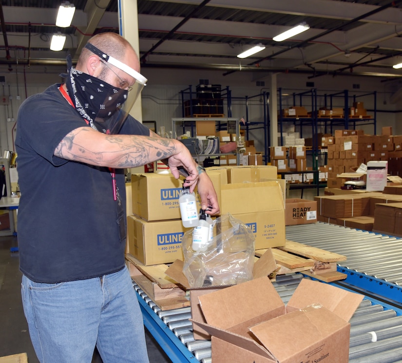 A man standing places two bottles into a box on a conveyor belt.