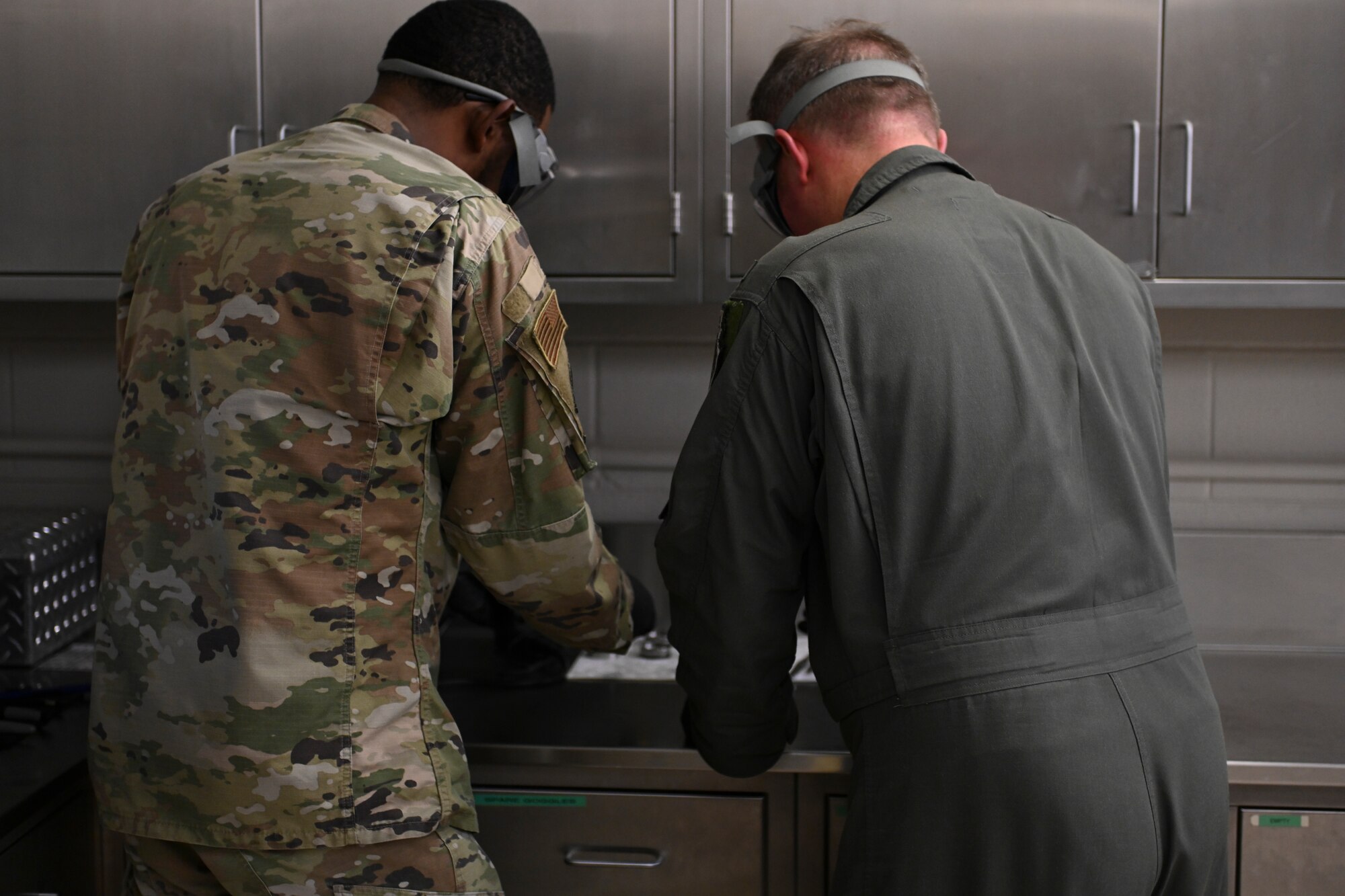 A photo of two Airmen leaning over a desk looking at fuel and water in small metal discs.