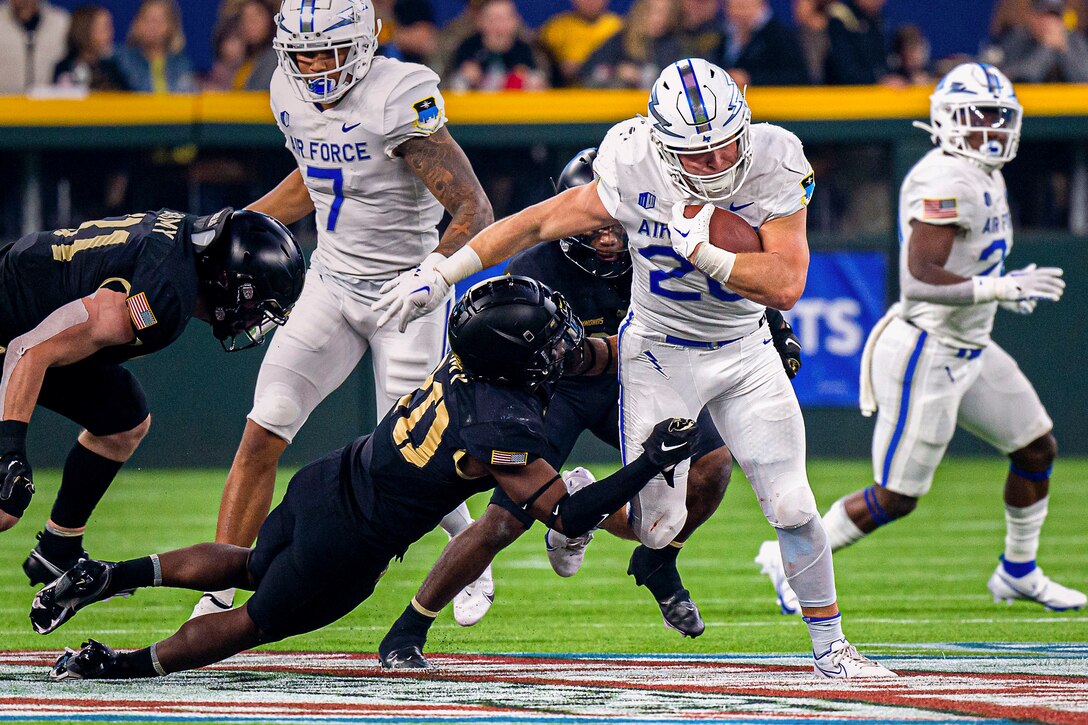 An Air Force football player runs while being tackled by Army football players.