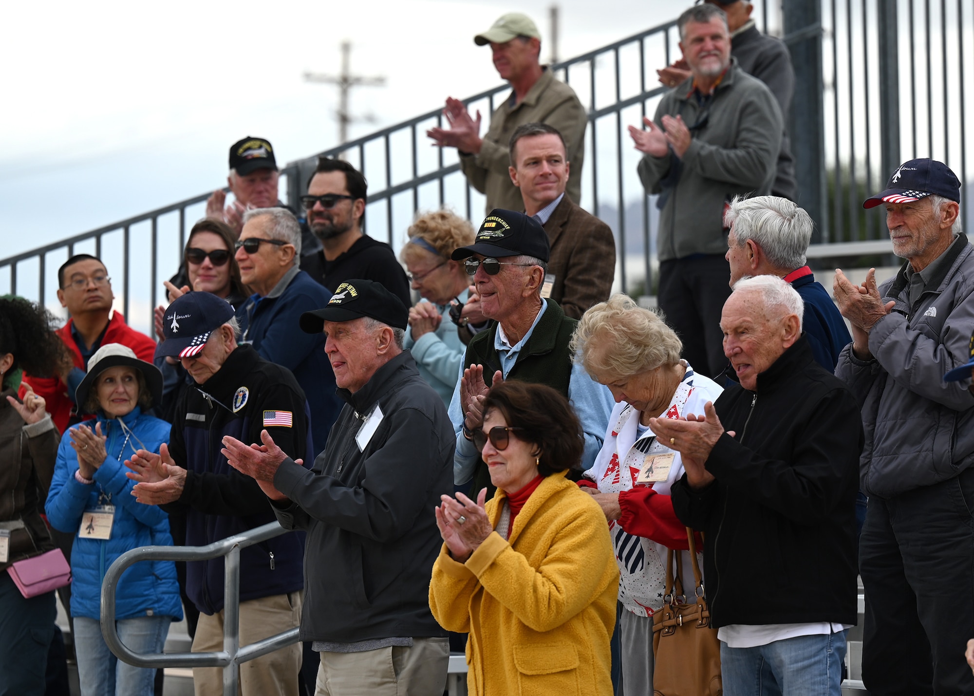 photo of a veterans and their family member standing on bleachers clapping
