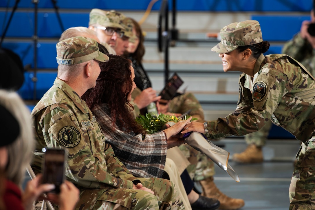 A standing airman smiles and presents a bouquet to a seated civilian.