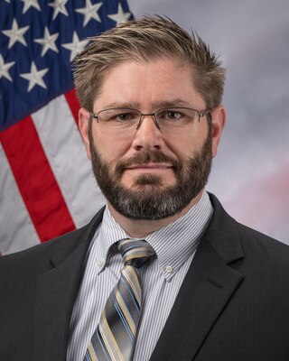A portrait of Dr. Colin Jay Williams with an American flag in the background