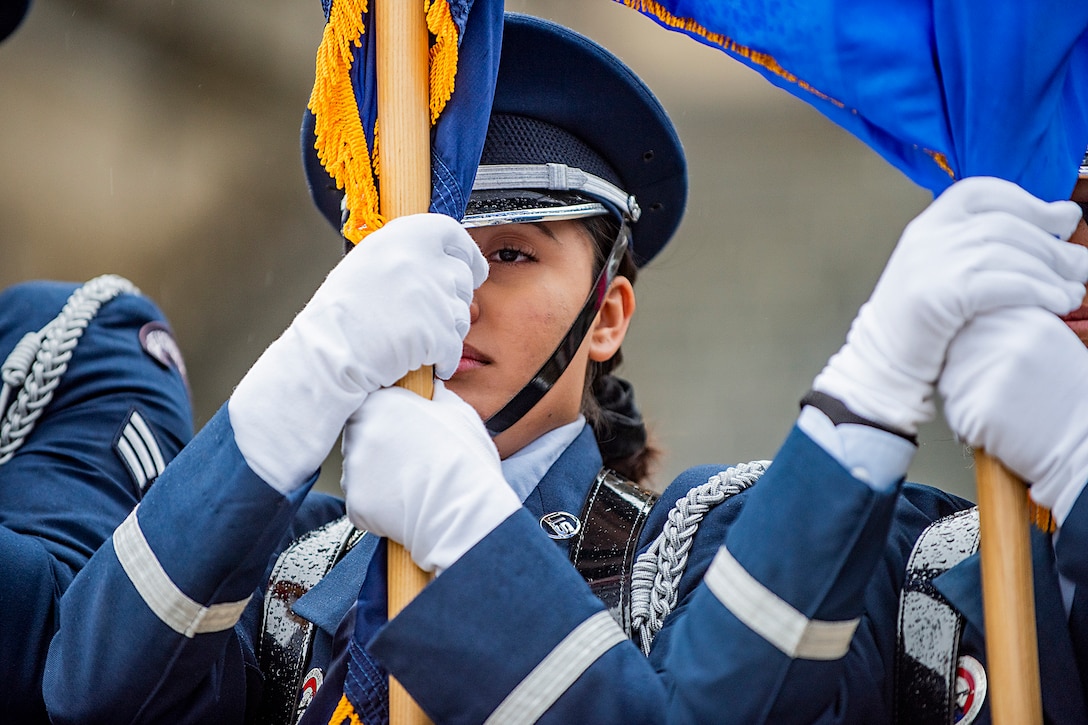 An airman holds the staff of a flag while standing at attention.