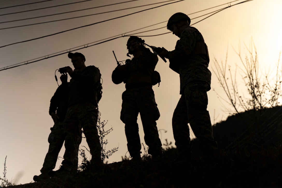 Four Marines stand next to each other on a hill under a sunlit silhouette.