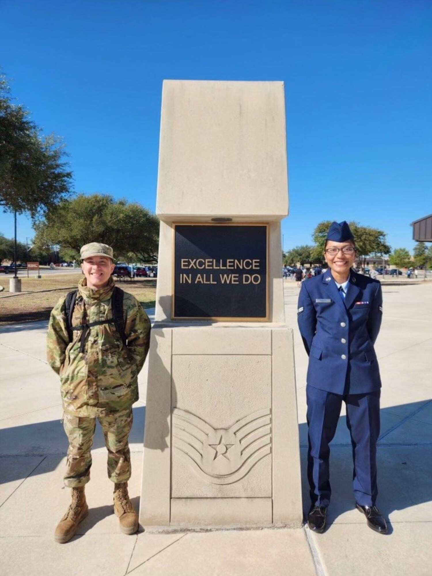 Airmen in uniform pose for a photo with a plaque between them.