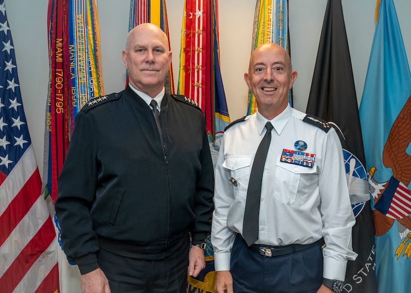 Two men pose for a photo in front of flags.