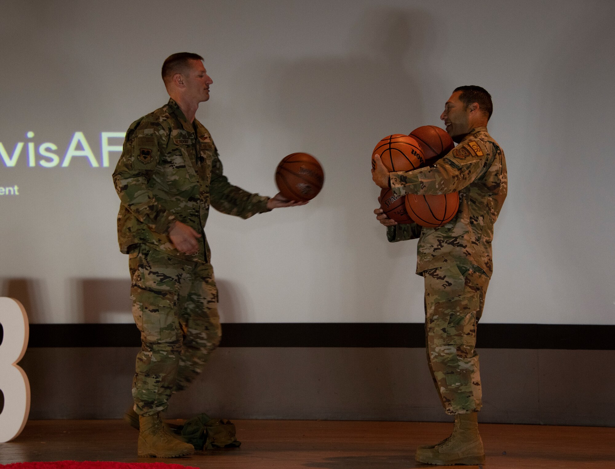 An Airman hands six basketballs to another Airmen and he struggles to carry them all.