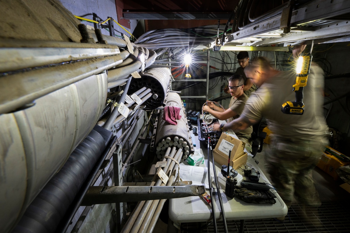 From front right, U.S. Air Force Staff Sgt. Christian Schroeder, U.S. Air Forces Central Command A 6/7 engineering and installation cable antenna systems, Staff Sgt. Andrew Winfield, AFCENT A 6/7 engineering and installation radar, airfield and weather systems technician, and Senior Airman Juan Olmos, 386th Expeditionary Communications Squadron cable antenna systems, splice strands of cable together at Ali Al Salem Air Base, Kuwait, Nov. 3, 2022. The team worked to splice 672 strands together in order to bolster communication capabilities for the installation. (U.S. Air Force photo by Staff Sgt. Dalton Williams)