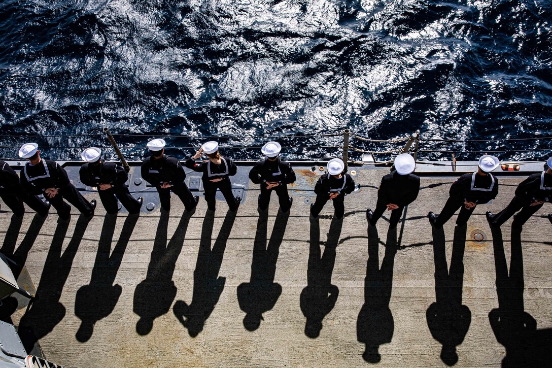 Sailors are seen from above standing in a line with their hands behind their backs.